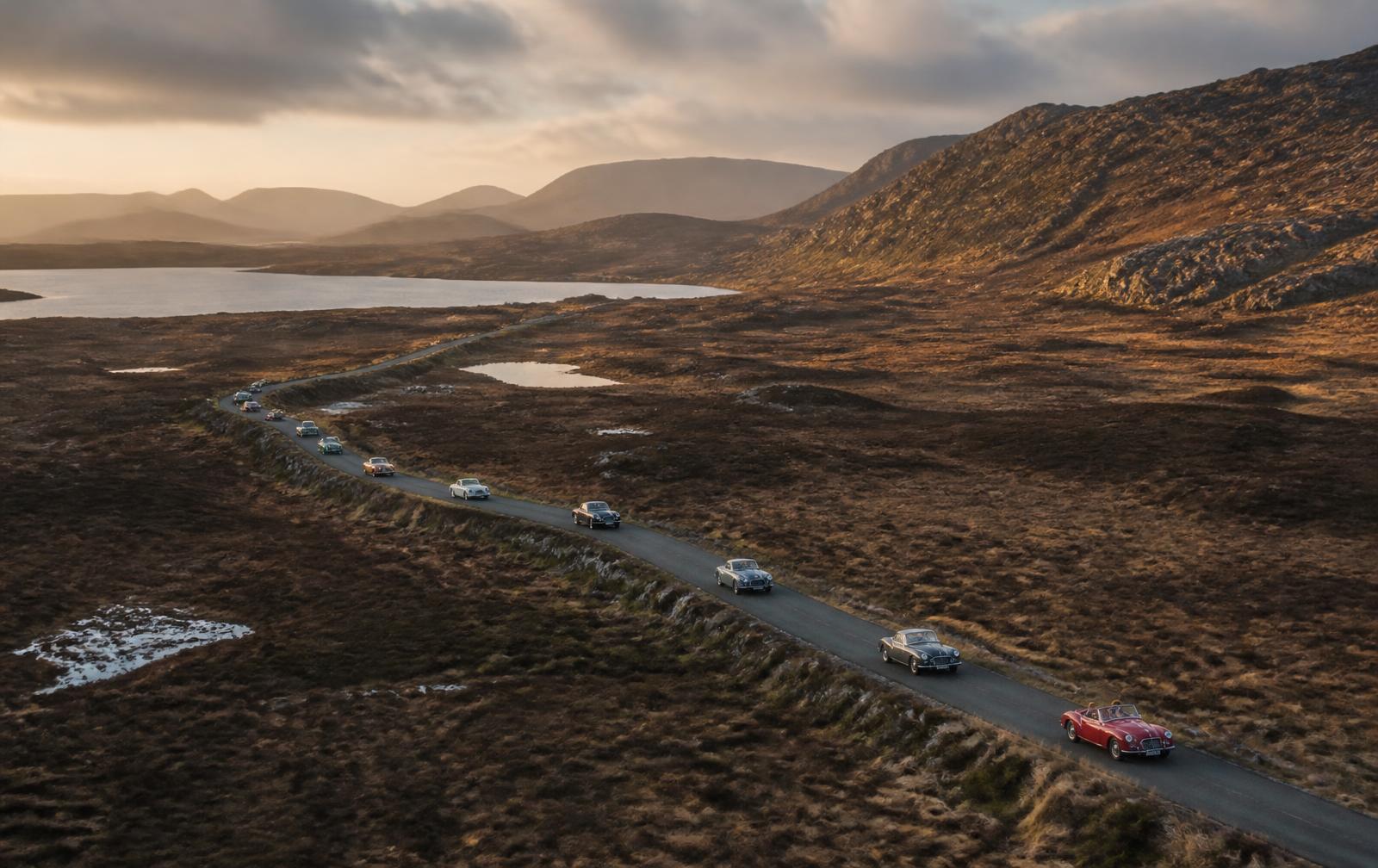 A convoy of classic sports cars crossing a remote Irish mountain pass at golden hour